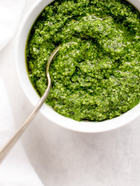 kale pesto in white bowl on white background with spoon