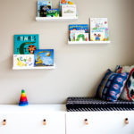 Playroom with white modern toy storage bench IKEA and floating white shelves with kids books