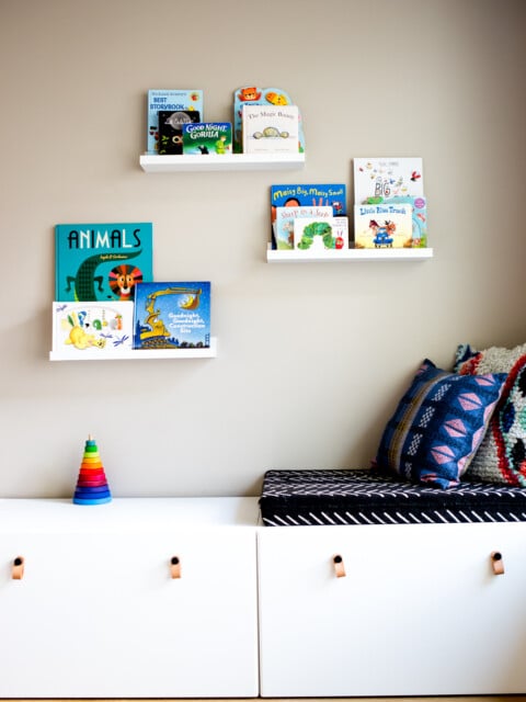 Playroom with white modern toy storage bench IKEA and floating white shelves with kids books