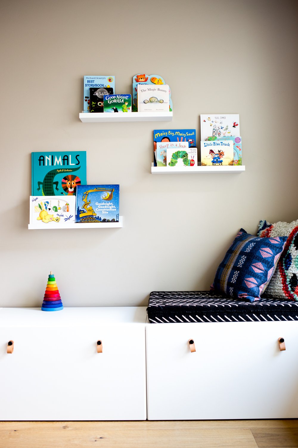 modern playroom with books on floating shelves and white storage drawers with bohemian and african mudcloth style cushions