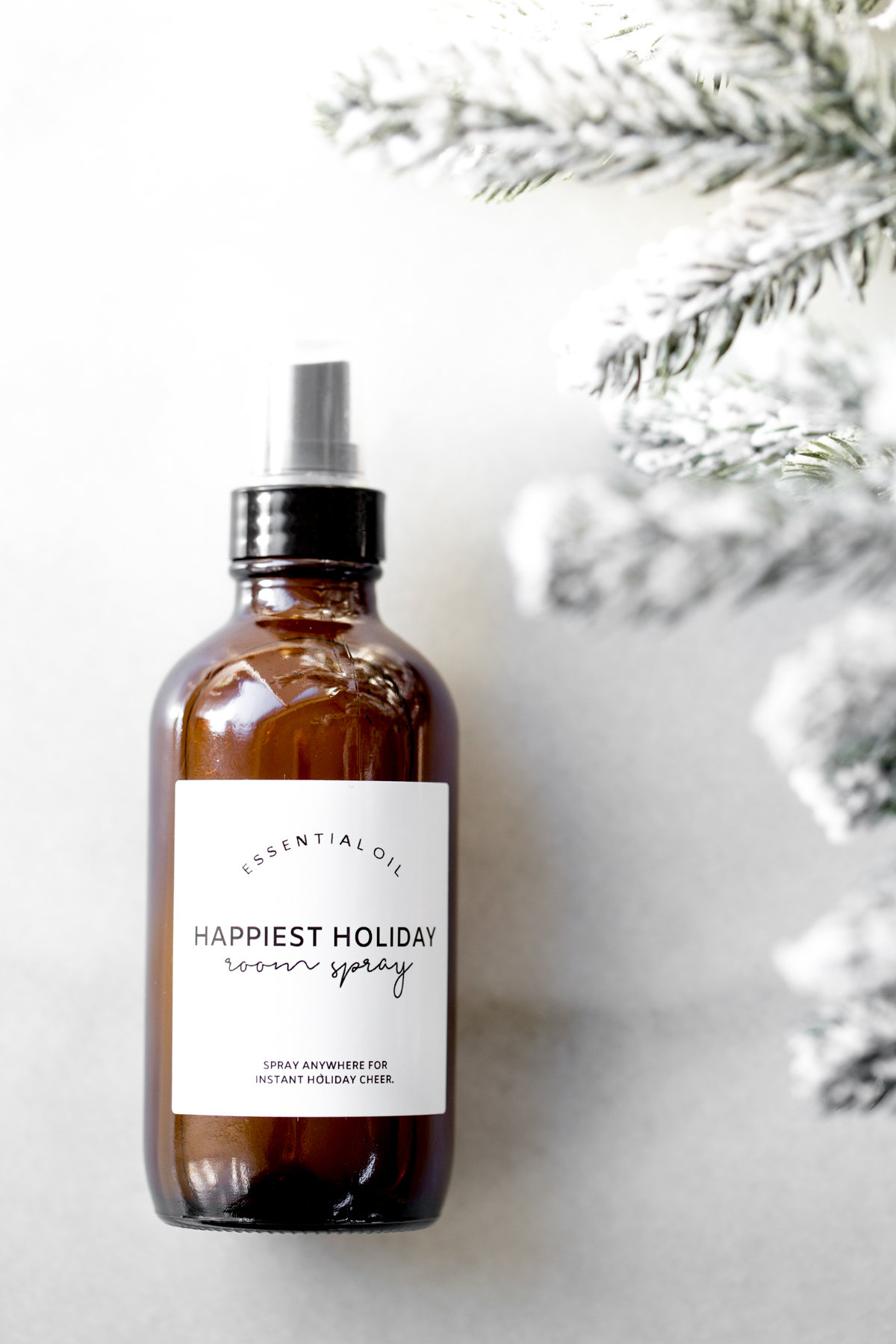 Bottle of holiday room spray on marble background with snow covered tree branches on the side