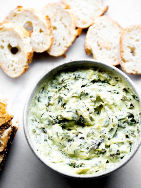 overhead photo of creamy instant pot spinach artichoke dip with sliced baguette on white marble background