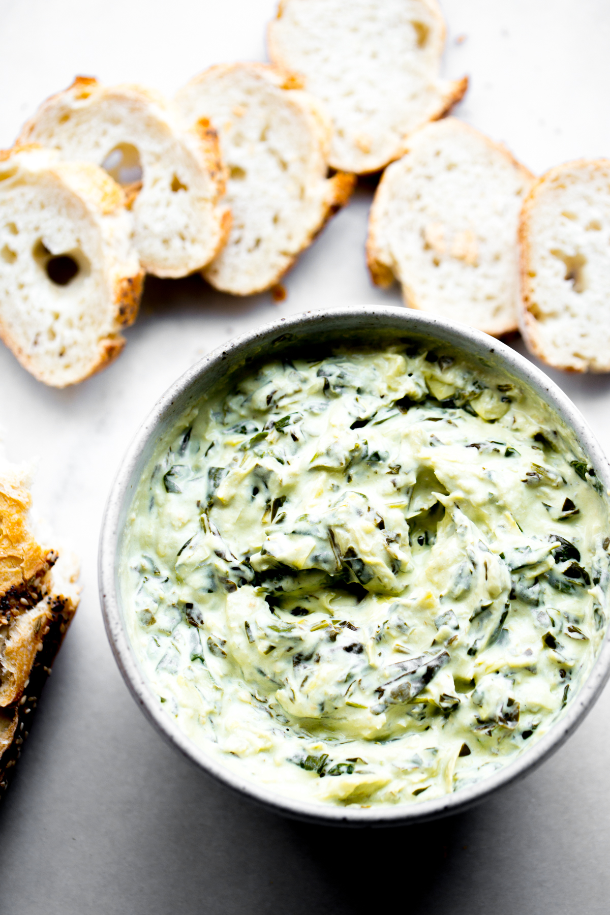 overhead photo of creamy instant pot spinach artichoke dip with sliced baguette on white marble background