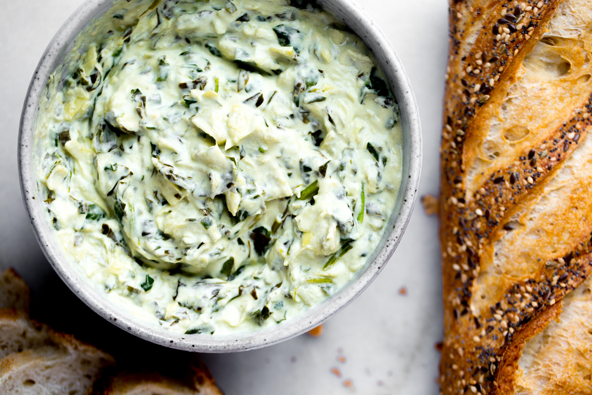 closeup overhead photo of spinach artichoke dip with a baguette on the side