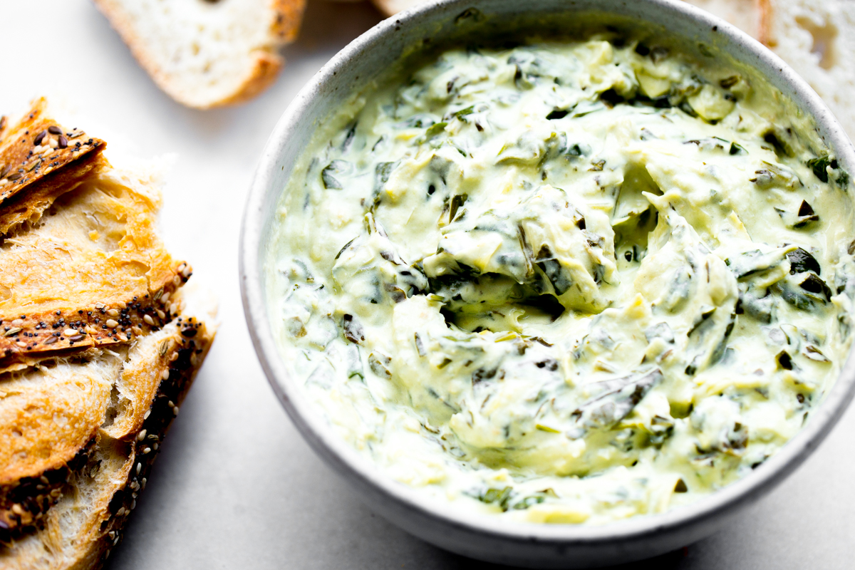 close up photo of pressure cooker spinach artichoke dip with sliced baguette on white marble background