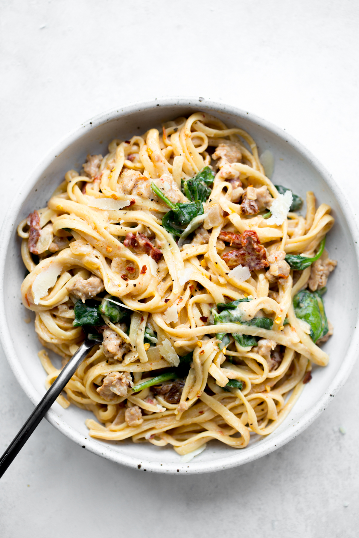 bowl of instant pot pasta with sausage spinach and sun-dried tomatoes on a white background