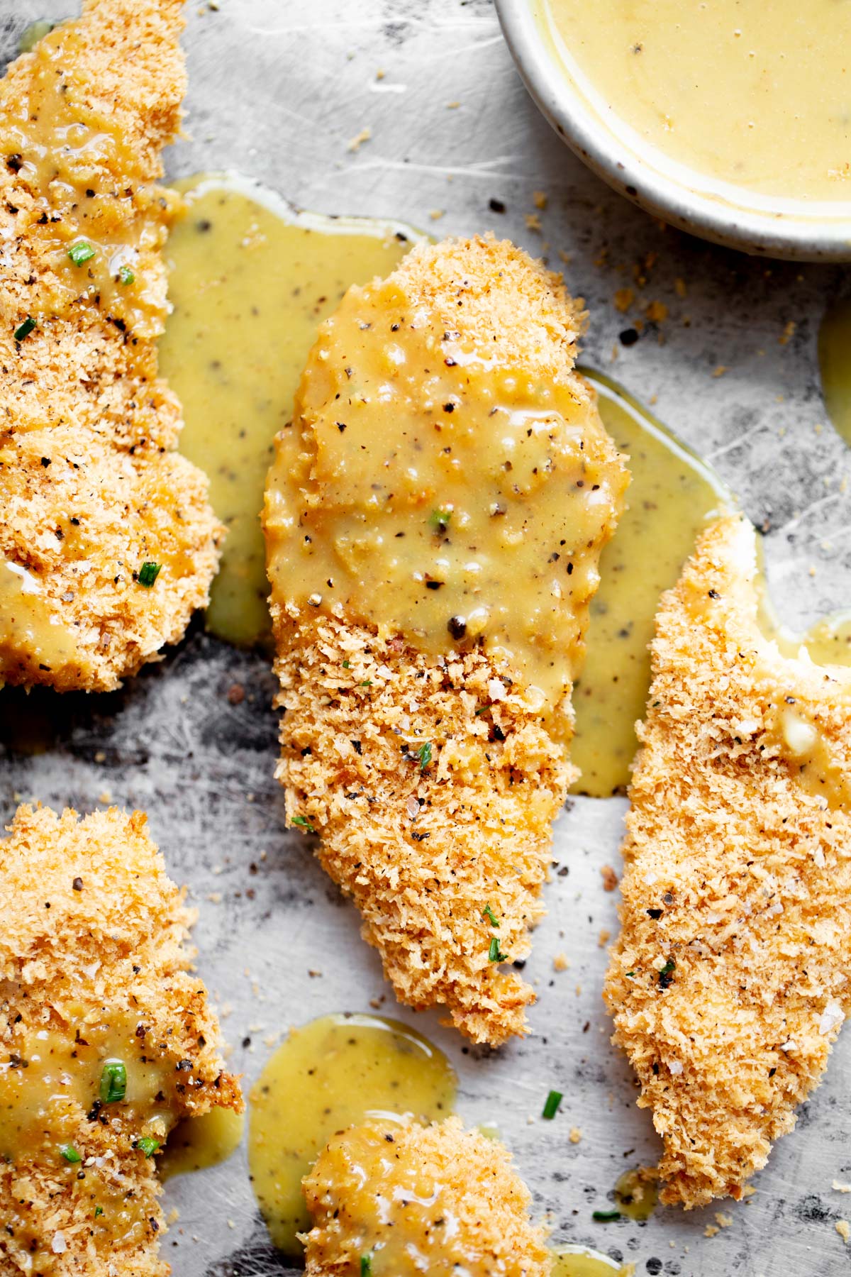 Overhead photo of baked chicken tenders drizzled with honey mustard sauce on a baking sheet