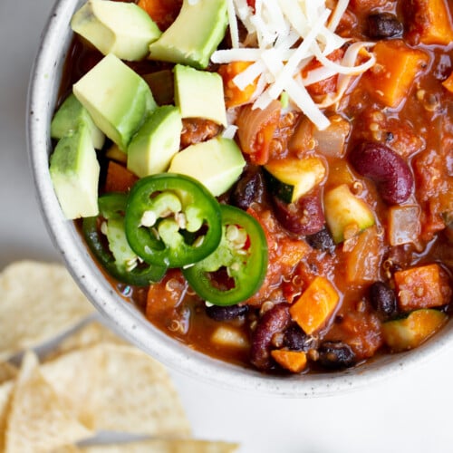 closeup overhead shot of a bowl of vegan vegetarian quinoa chili on marble background with tortilla chips and cilantro