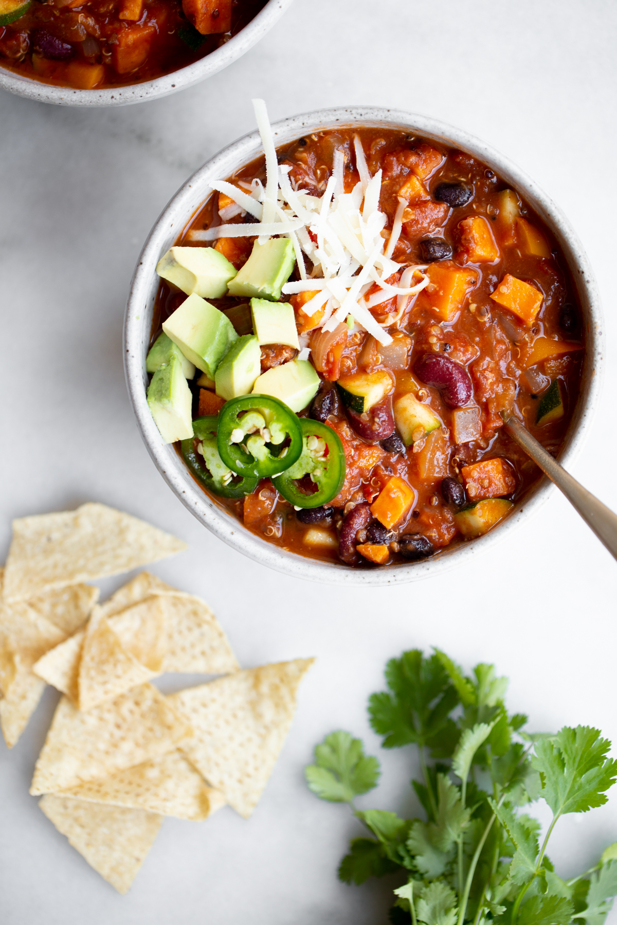overhead shot of a bowl of vegan vegetarian sweet potato quinoa chili on marble background with tortilla chips and cilantro