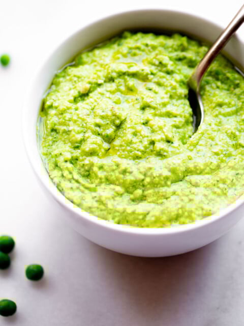 45 degree angle of a backlit bowl of pea pesto with a spoon on a white marble background