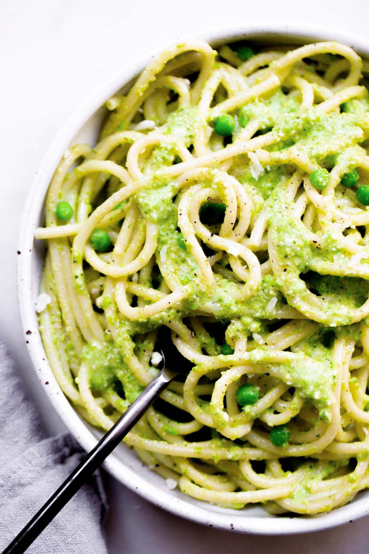 overhead of a bowl of spaghetti coated in green pea pesto with a fork on a white marble background