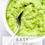 overhead photo of a bowl of pea pesto with a spoon on a white marble background with title text overlay