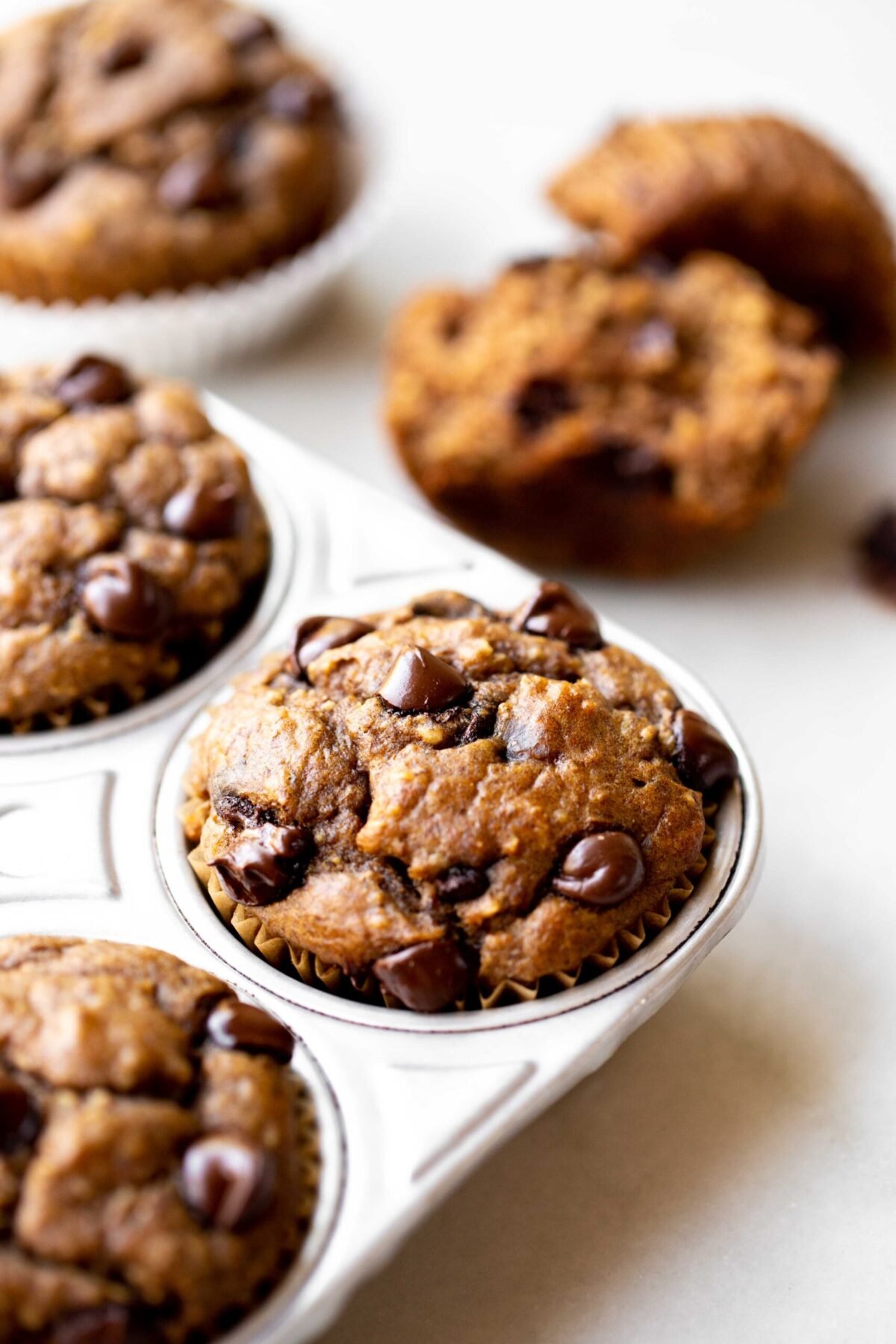 closeup photo at 45 degree angle of freshly baked healthy chocolate chip banana muffins in an aluminum muffin pan on a light gray marble background