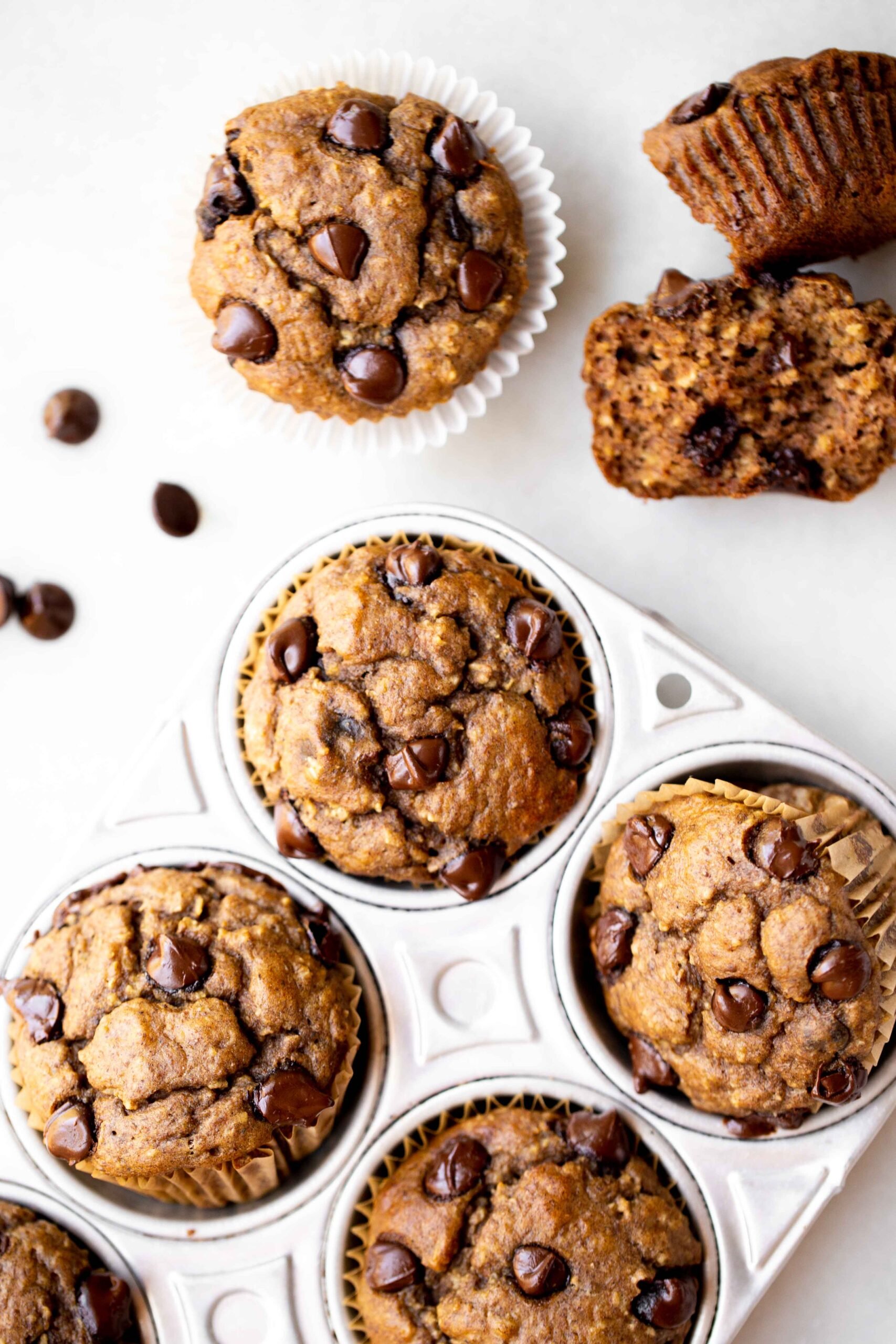 overhead photo of freshly baked healthy chocolate chip banana muffins in an aluminum muffin pan with milk and chocolate chips in the background