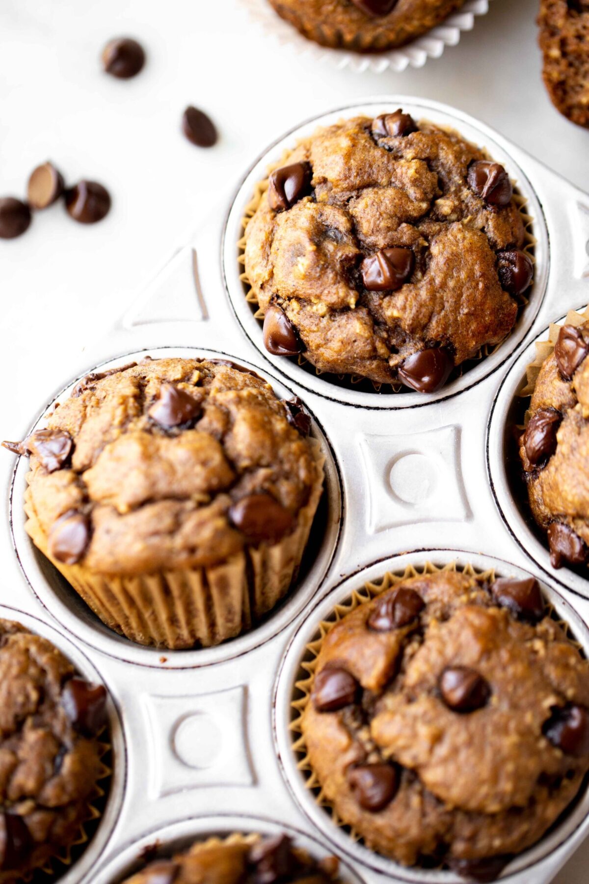 closeup photo at 45 degree angle of freshly baked chocolate chip banana muffins in an aluminum muffin pan on a light gray marble background