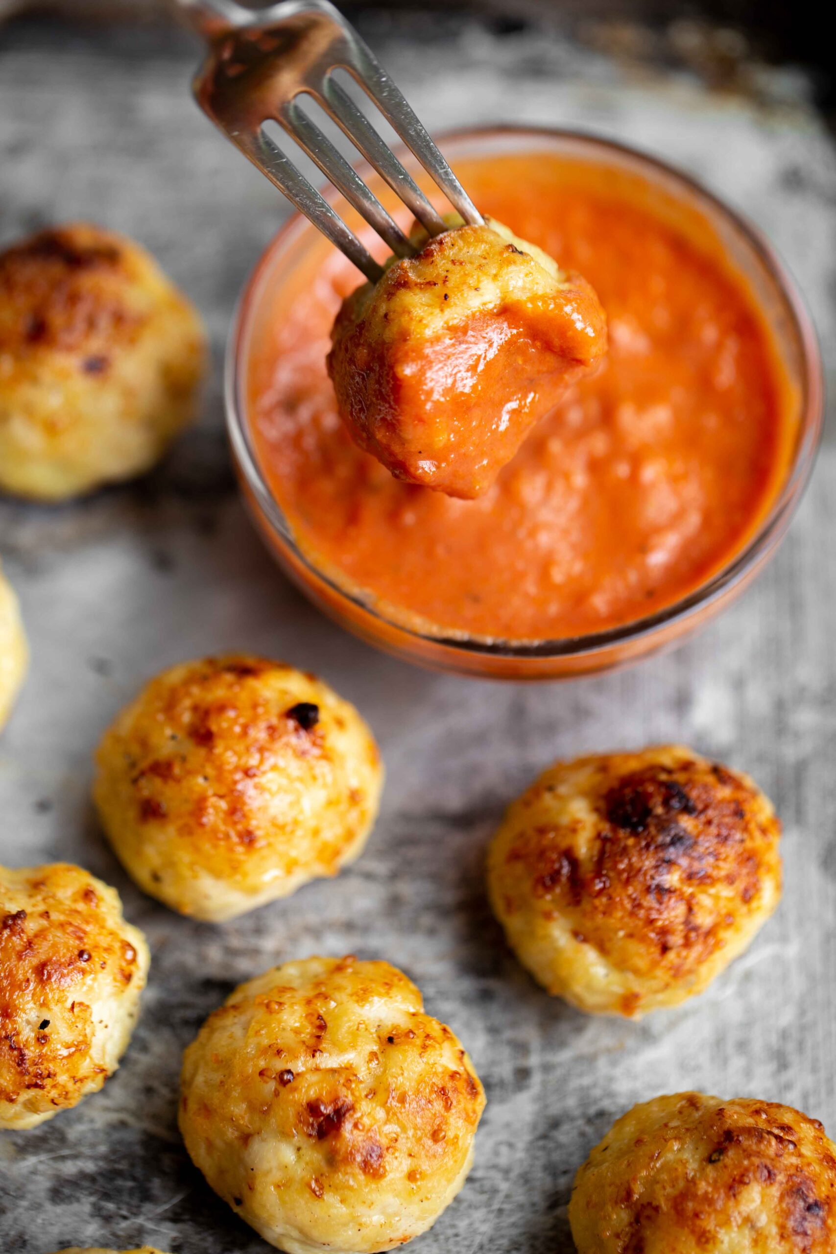 closeup photo of a bitten chicken meatball on a fork dipped in tomato sauce