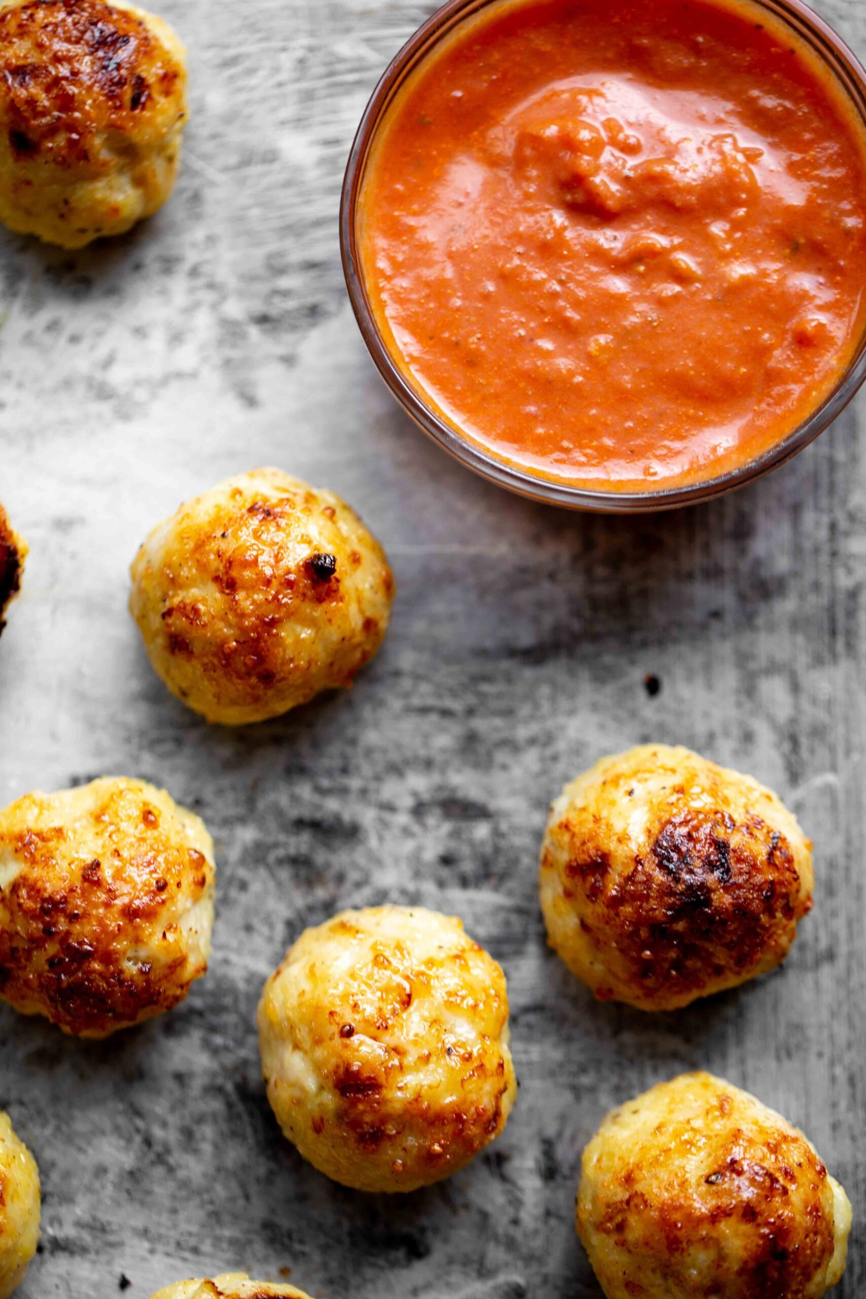 Overhead closeup of baked chicken meatballs on a sheet pan with red marinara sauce