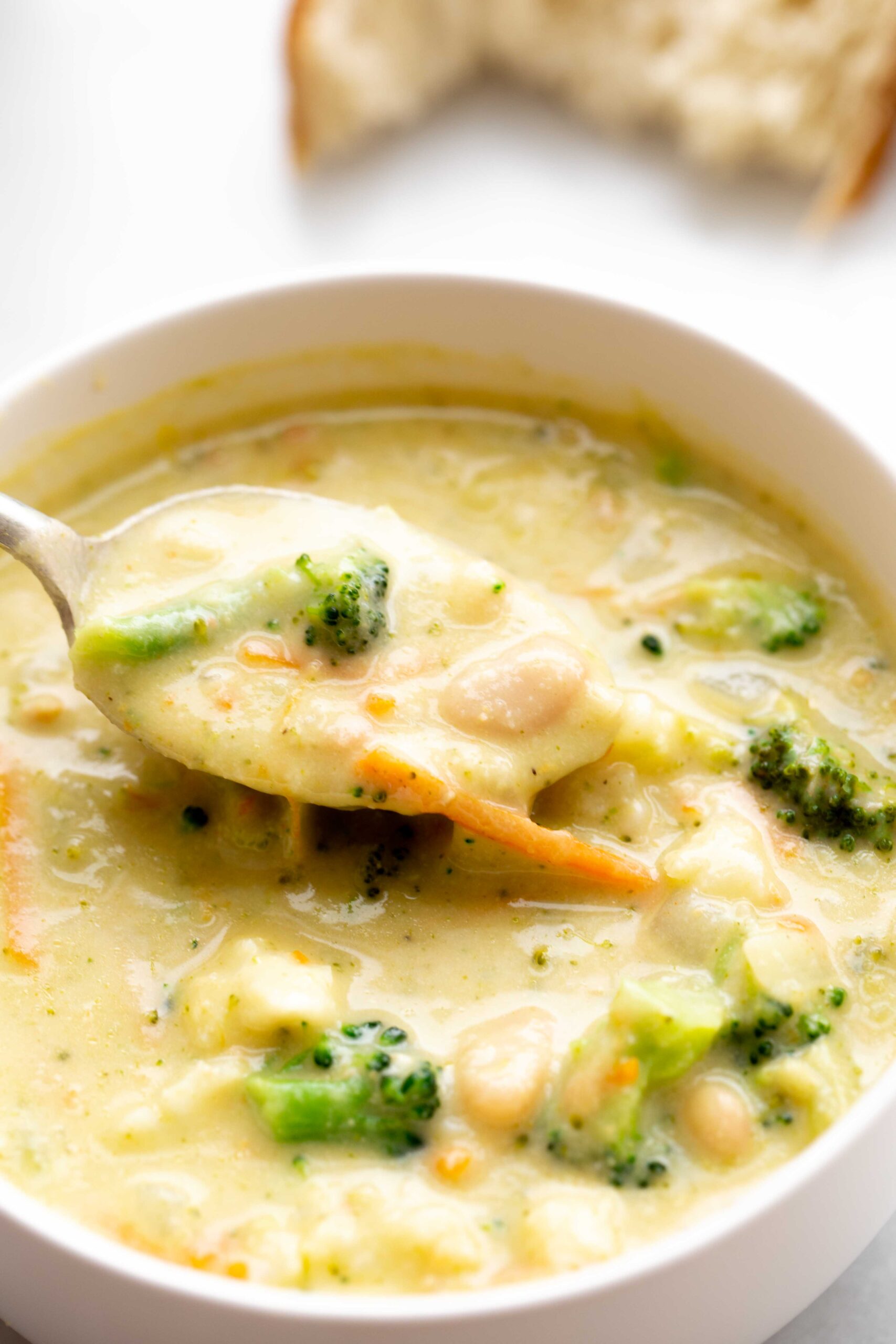 closeup photo of a spoonful of creamy broccoli cauliflower cheese soup with carrot and white beans