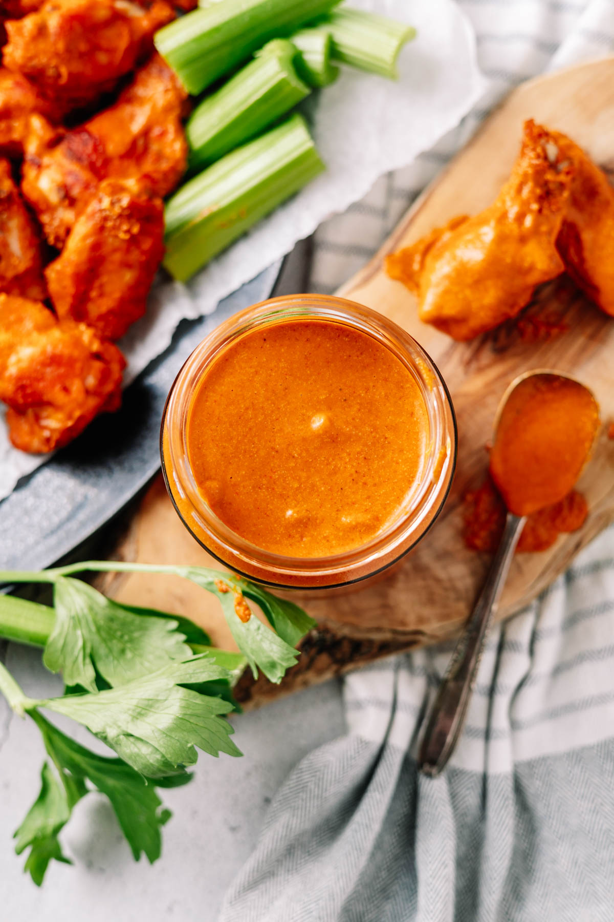 An overhead photo of homemade Buffalo sauce with a saucy spoon and wings in the background