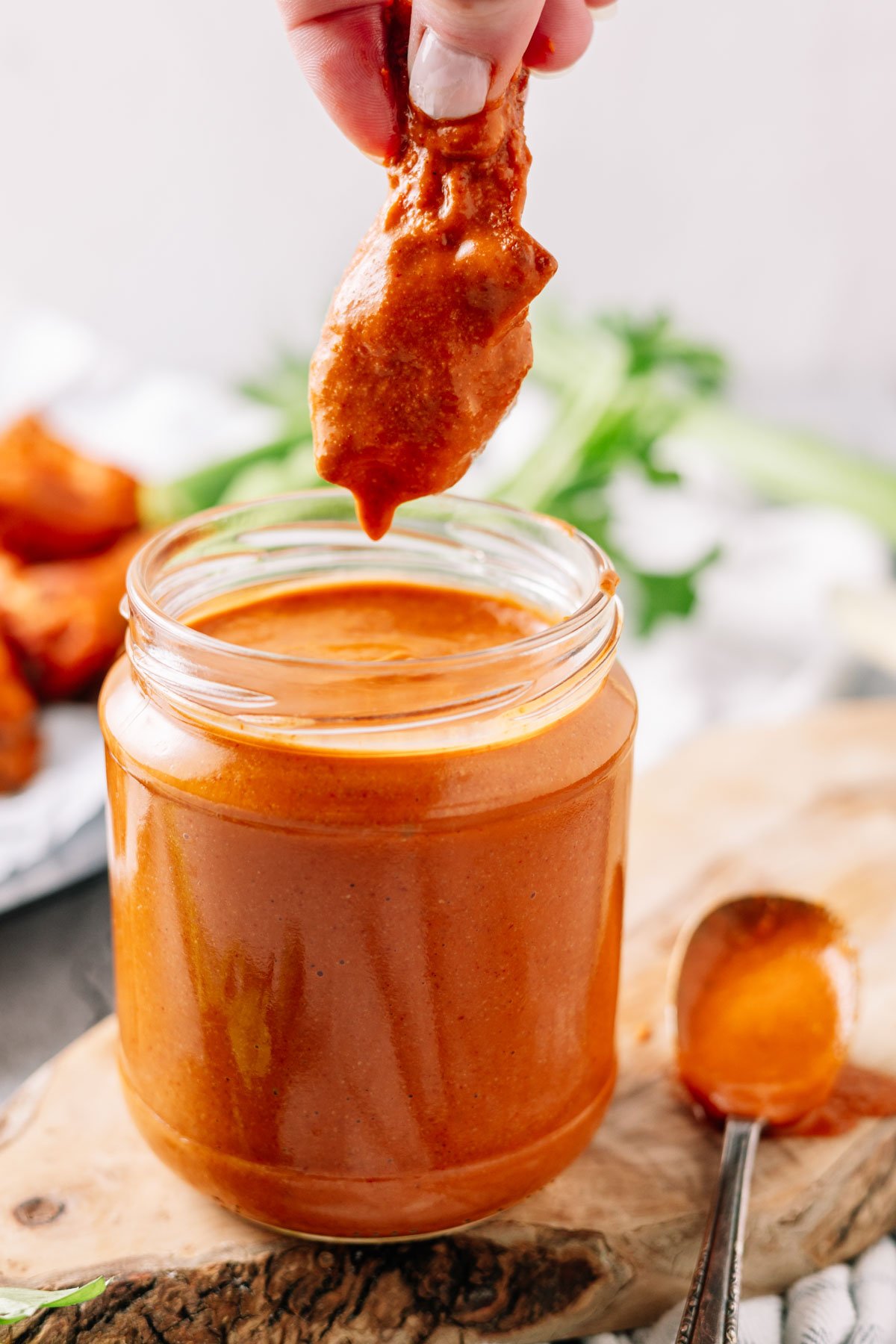 A chicken wing being dipped into a glass jar of thick Buffalo sauce 