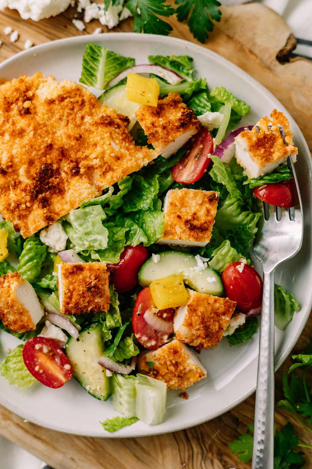 Crispy chicken cutlet sliced and served on top of a salad with tomatoes, cucumber, and bell pepper
