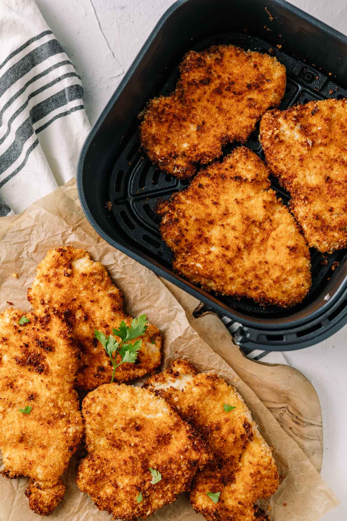 Top-down image crispy, golden chicken cutlets in air fryer basket with some on the table next to it
