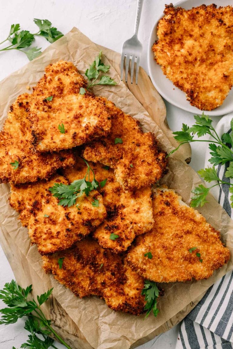 a plate of crispy, golden air fryer chicken cutlets on brown paper and cutting board with white background