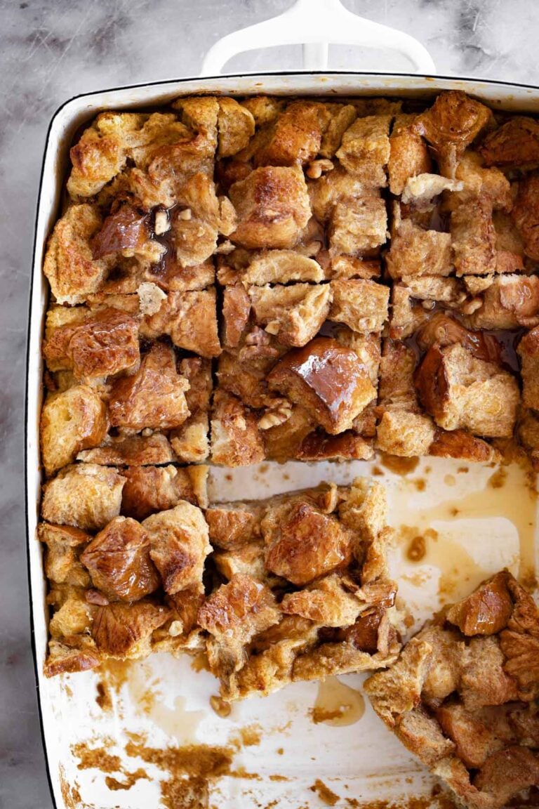 Closeup overhead photo of brioche French toast casserole sliced in a white ceramic baking dish on marble background