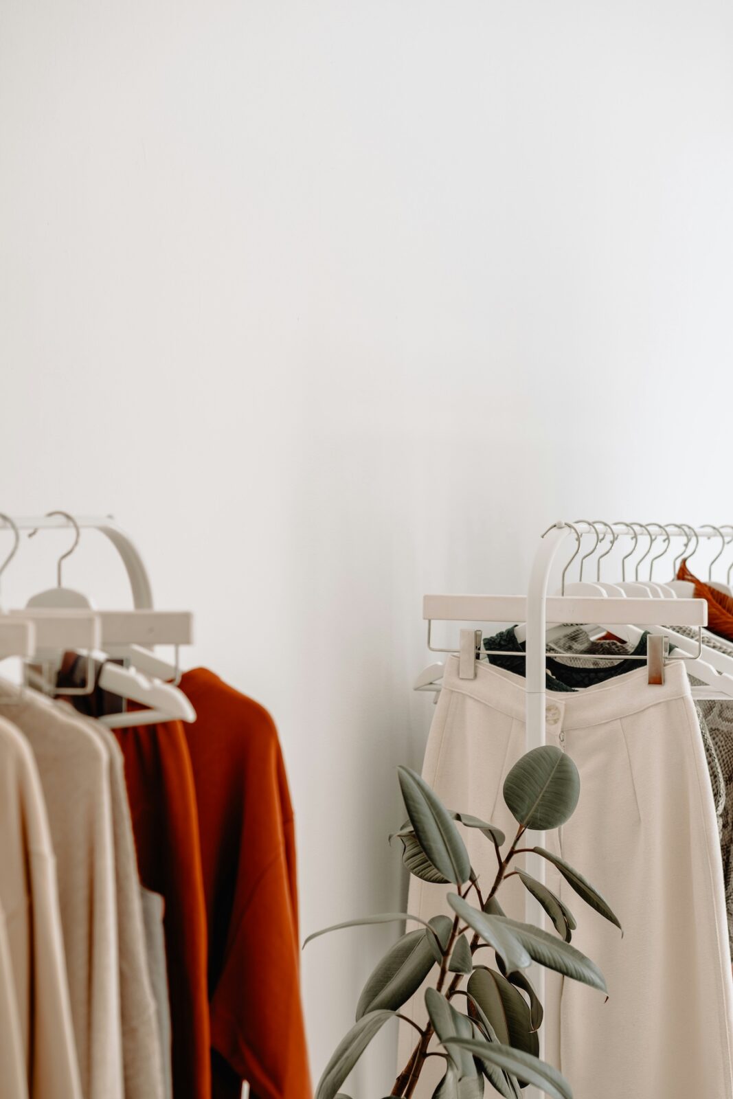A closeup image of minimalist womens clothing on 2 white rolling racks in a bright and airy shop