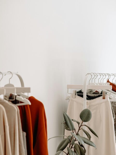 A closeup image of minimalist womens clothing on 2 white rolling racks in a bright and airy shop