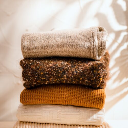 Fall sweaters stacked on a textured background