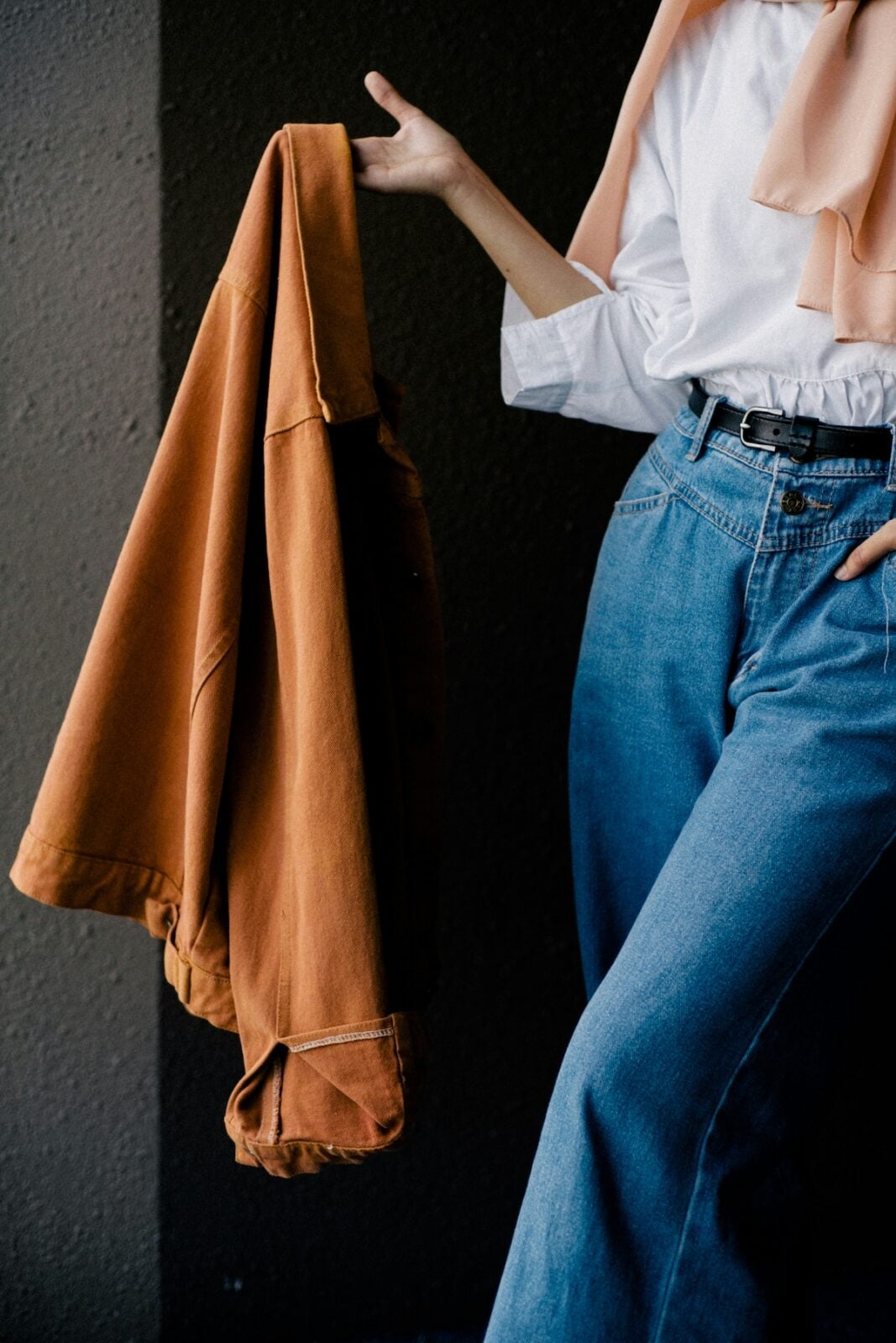 Rust colored jacket layered over a white blouse and peach scarf with wide-leg jeans, a fall capsule wardrobe outfit idea