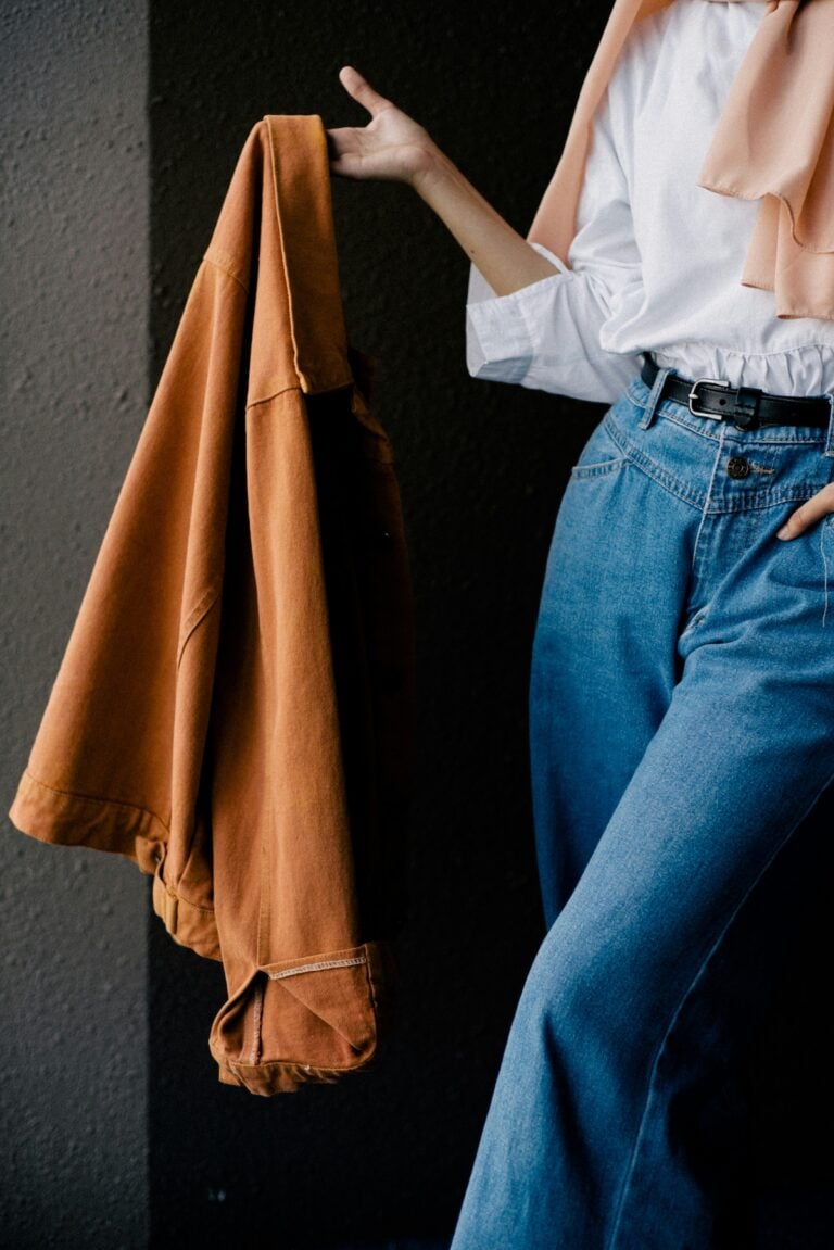Rust colored jacket layered over a white blouse and peach scarf with wide-leg jeans, a fall capsule wardrobe outfit idea