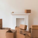 A minimalist white living room with wood floors covered in big moving boxes