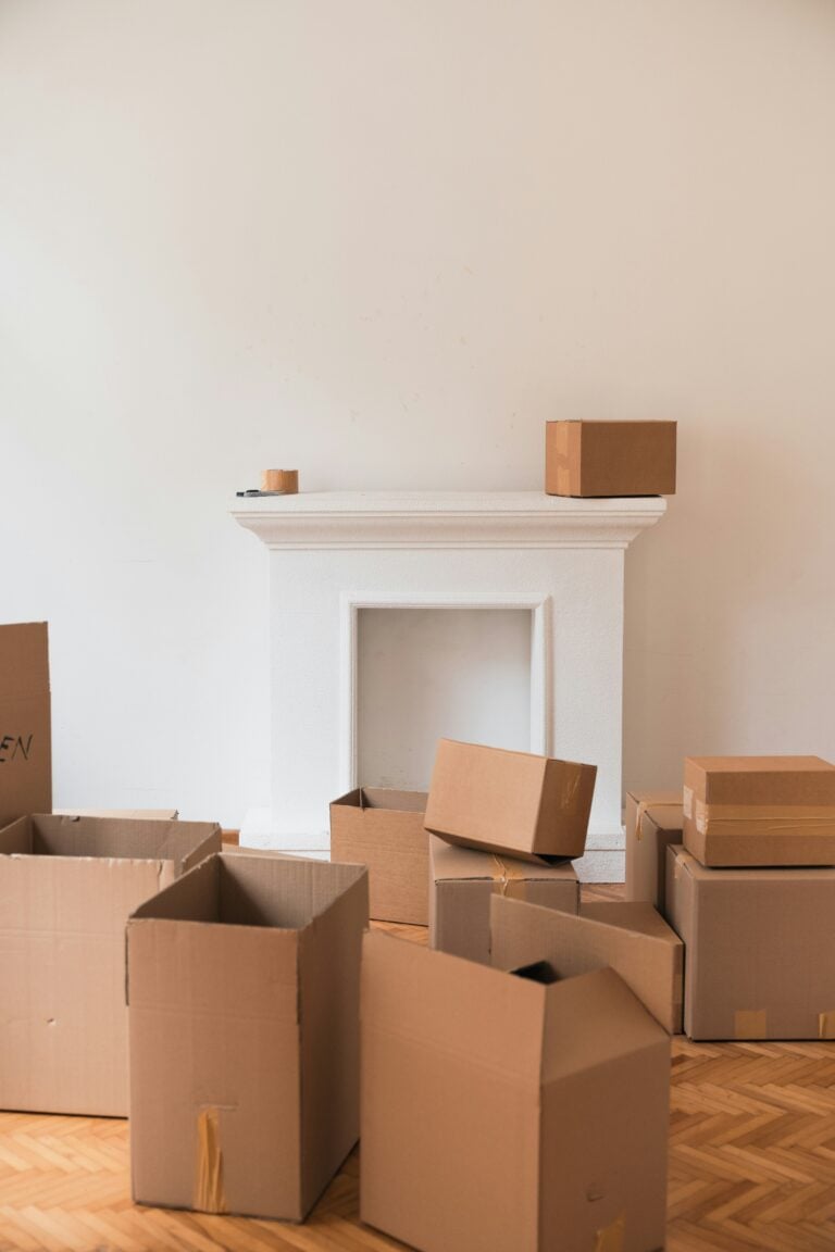 A minimalist white living room with wood floors covered in big moving boxes