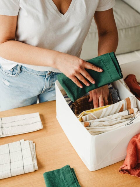 Closeup of a woman folding towels and placing them neatly into a storage bin, illustrating simple home organizing tips.