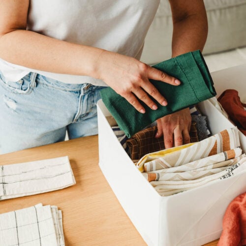 Closeup of a woman folding towels and placing them neatly into a storage bin, illustrating simple home organizing tips.