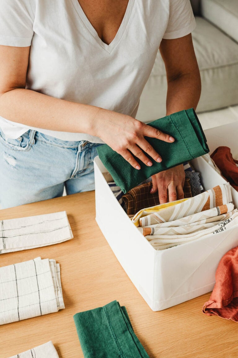 Closeup of a woman folding towels and placing them neatly into a storage bin, illustrating simple home organizing tips.