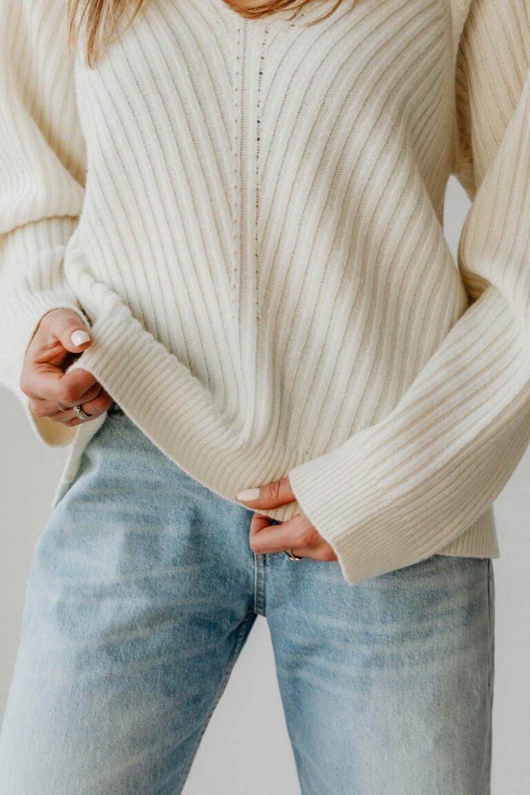 A woman wearing a cream ribbed sweater and light-wash jeans, styled as a simple capsule wardrobe outfit with a minimalist, casual look.